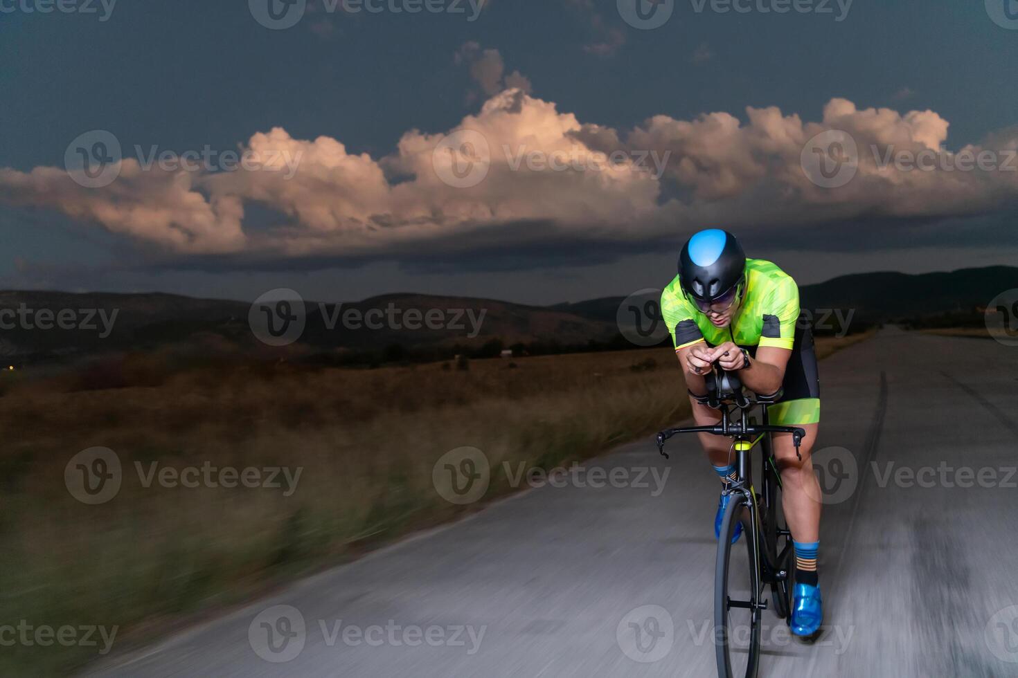 A triathlete rides his bike in the darkness of night, pushing himself to prepare for a marathon. The contrast between the darkness and the light of his bike creates a sense of drama and highlights the photo