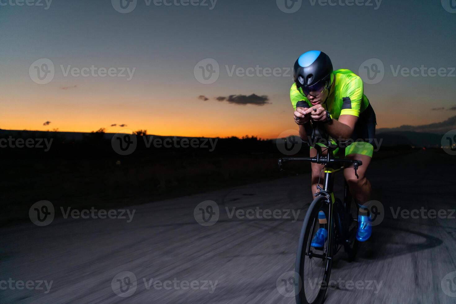A triathlete rides his bike in the darkness of night, pushing himself to prepare for a marathon. The contrast between the darkness and the light of his bike creates a sense of drama and highlights the photo