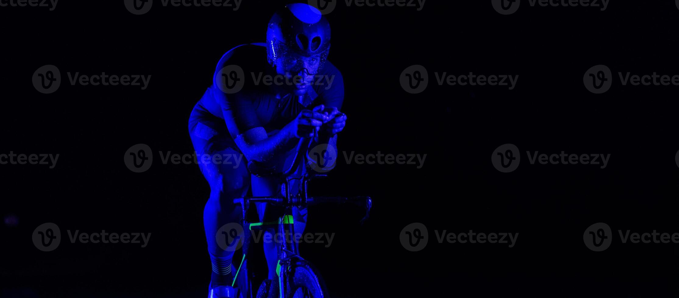 A triathlete rides his bike in the darkness of night, pushing himself to prepare for a marathon. The contrast between the darkness and the light of his bike creates a sense of drama and highlights the photo