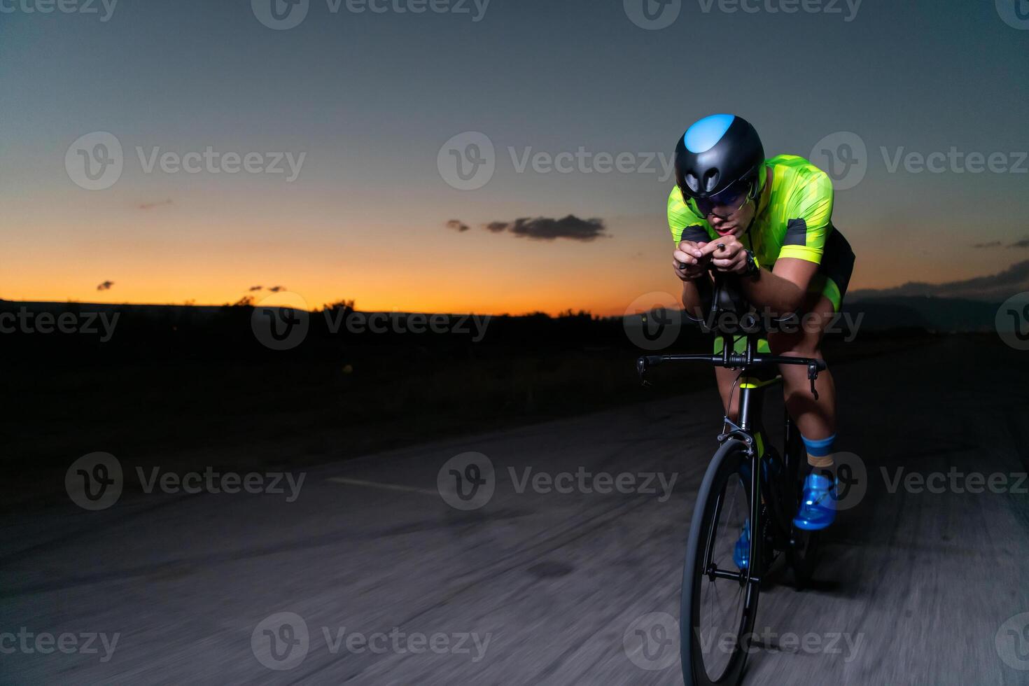 A triathlete rides his bike in the darkness of night, pushing himself to prepare for a marathon. The contrast between the darkness and the light of his bike creates a sense of drama and highlights the photo