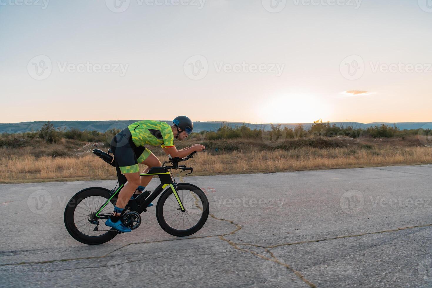 Triathlete riding his bicycle during sunset, preparing for a marathon. The warm colors of the sky provide a beautiful backdrop for his determined and focused effort. photo