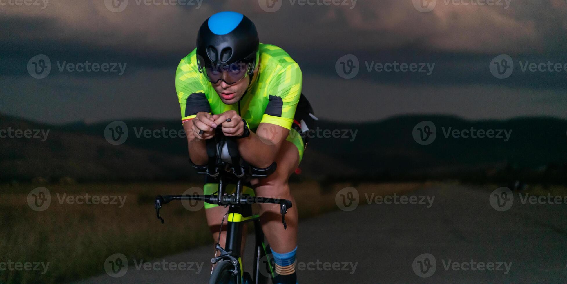 A triathlete rides his bike in the darkness of night, pushing himself to prepare for a marathon. The contrast between the darkness and the light of his bike creates a sense of drama and highlights the photo