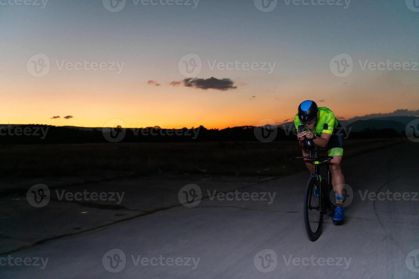 A triathlete rides his bike in the darkness of night, pushing himself to prepare for a marathon. The contrast between the darkness and the light of his bike creates a sense of drama and highlights the photo