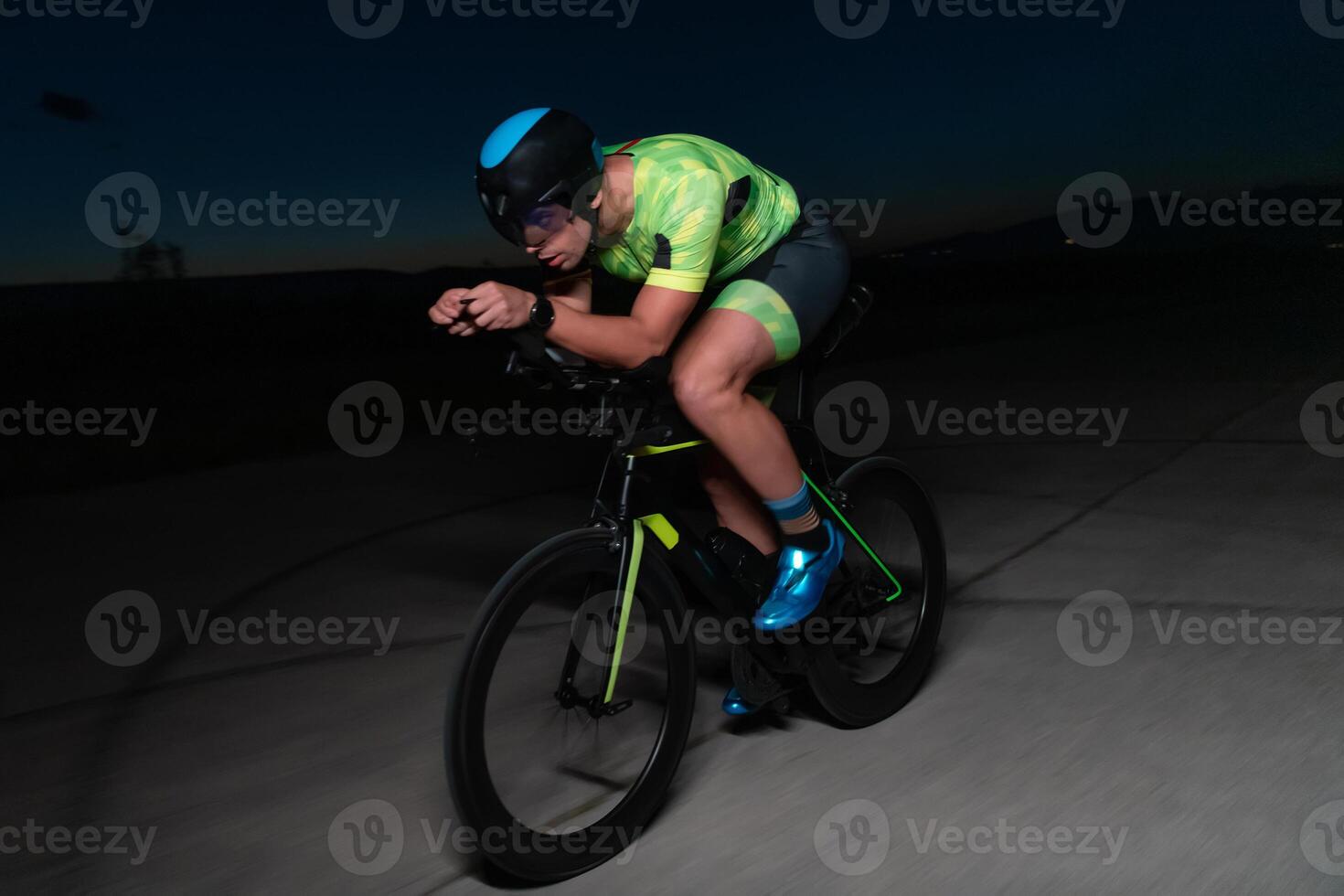 A triathlete rides his bike in the darkness of night, pushing himself to prepare for a marathon. The contrast between the darkness and the light of his bike creates a sense of drama and highlights the photo
