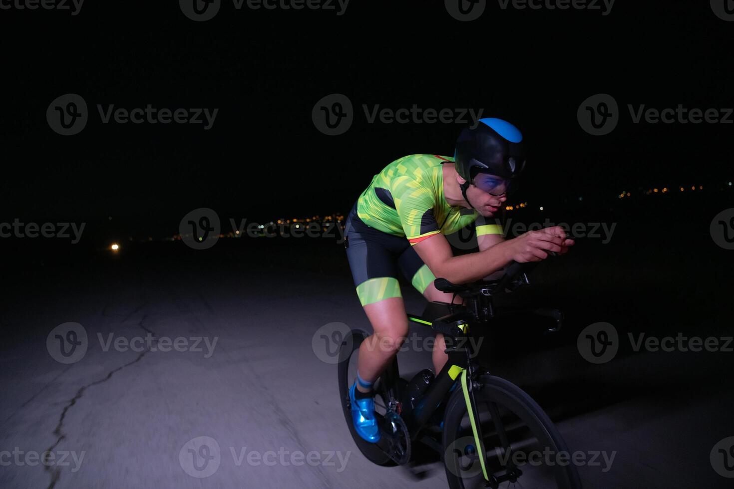 A triathlete rides his bike in the darkness of night, pushing himself to prepare for a marathon. The contrast between the darkness and the light of his bike creates a sense of drama and highlights the photo