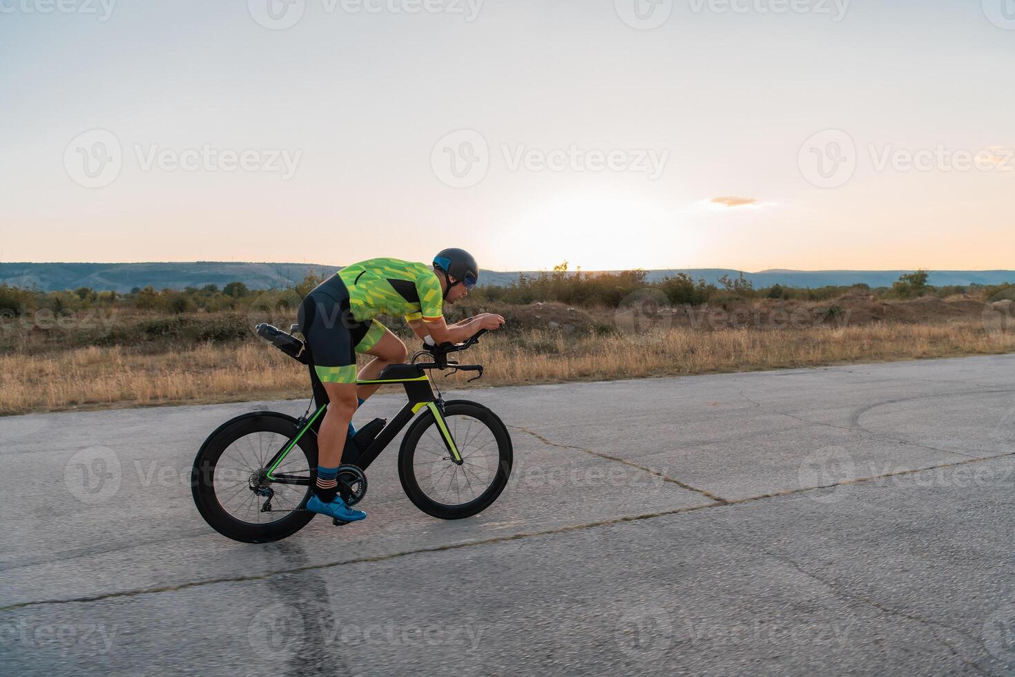 Triathlete riding his bicycle during sunset, preparing for a marathon. The warm colors of the sky provide a beautiful backdrop for his determined and focused effort. photo