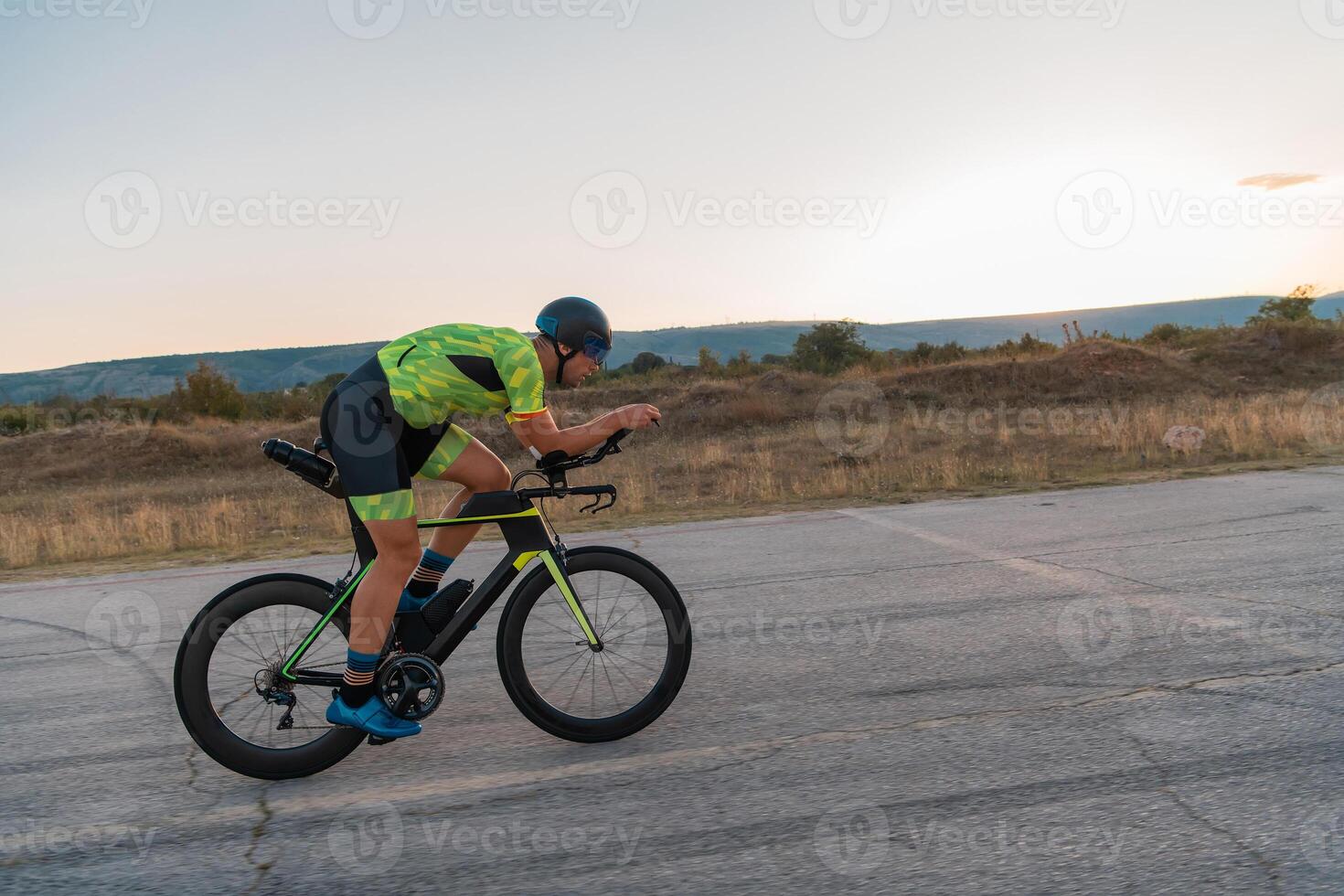 Triathlete riding his bicycle during sunset, preparing for a marathon. The warm colors of the sky provide a beautiful backdrop for his determined and focused effort. photo