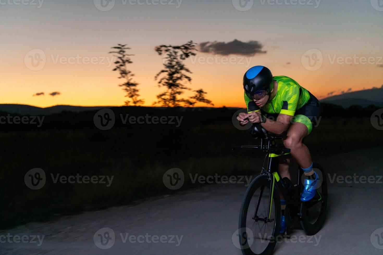 A triathlete rides his bike in the darkness of night, pushing himself to prepare for a marathon. The contrast between the darkness and the light of his bike creates a sense of drama and highlights the photo