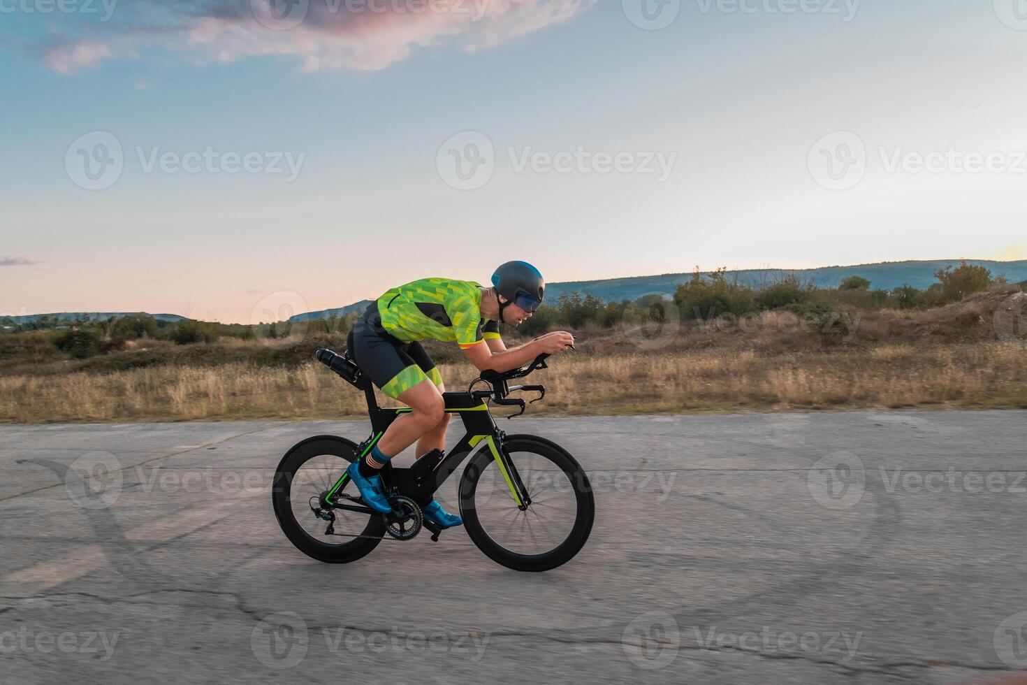 Triathlete riding his bicycle during sunset, preparing for a marathon. The warm colors of the sky provide a beautiful backdrop for his determined and focused effort. photo