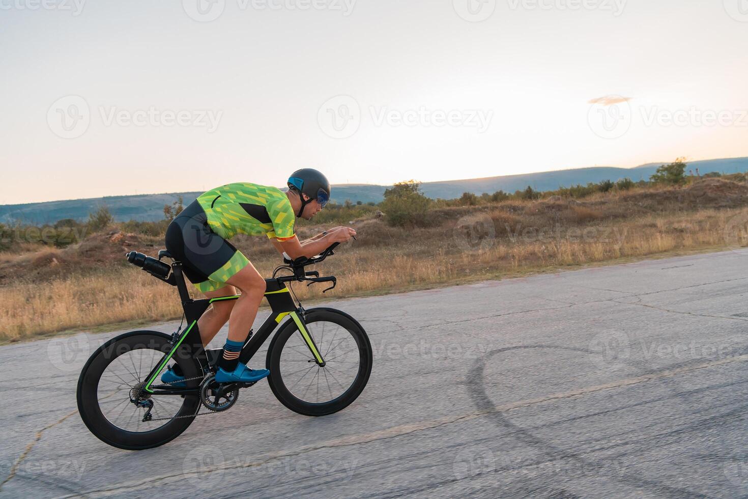 Triathlete riding his bicycle during sunset, preparing for a marathon. The warm colors of the sky provide a beautiful backdrop for his determined and focused effort. photo
