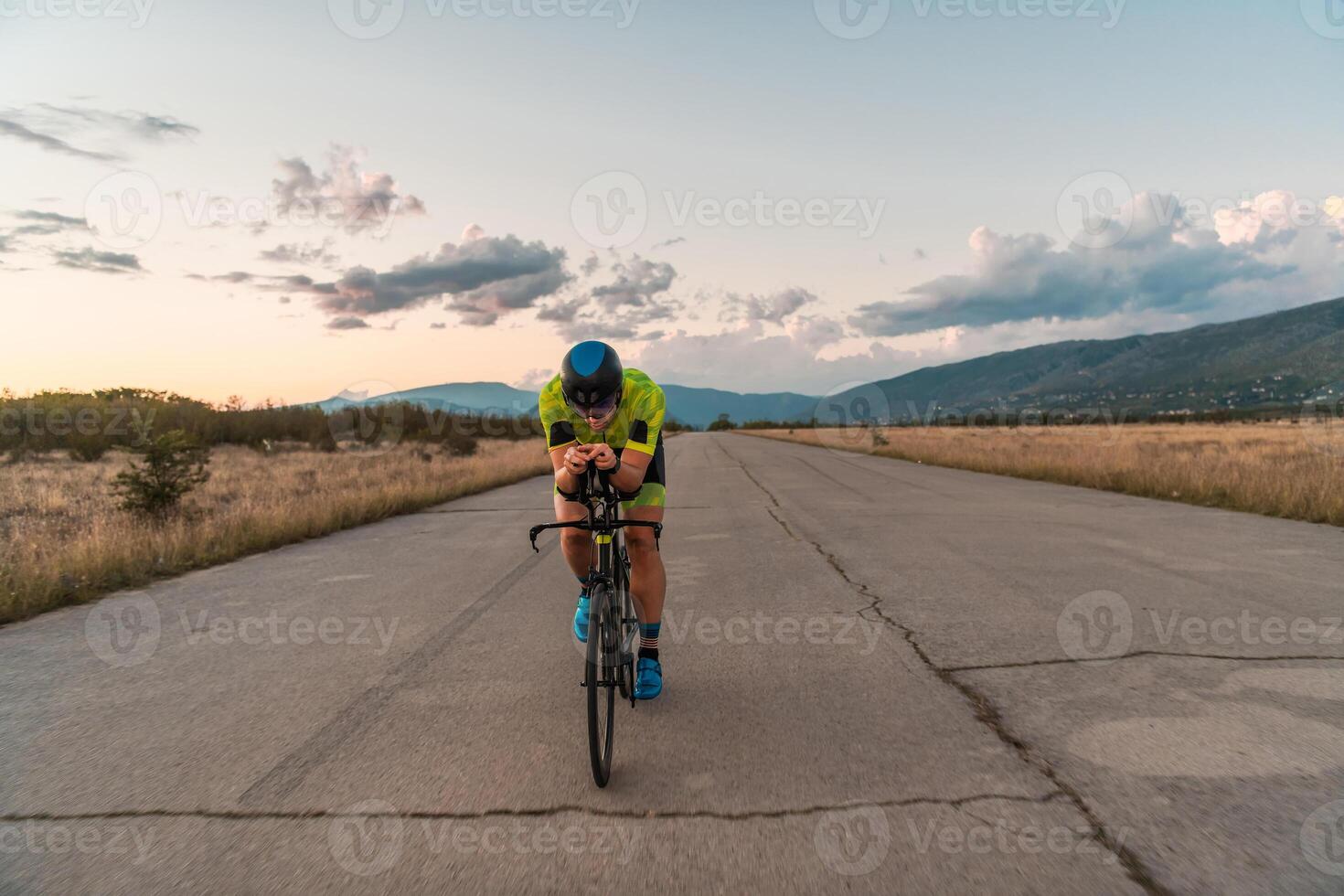 Triathlete riding his bicycle during sunset, preparing for a marathon. The warm colors of the sky provide a beautiful backdrop for his determined and focused effort. photo