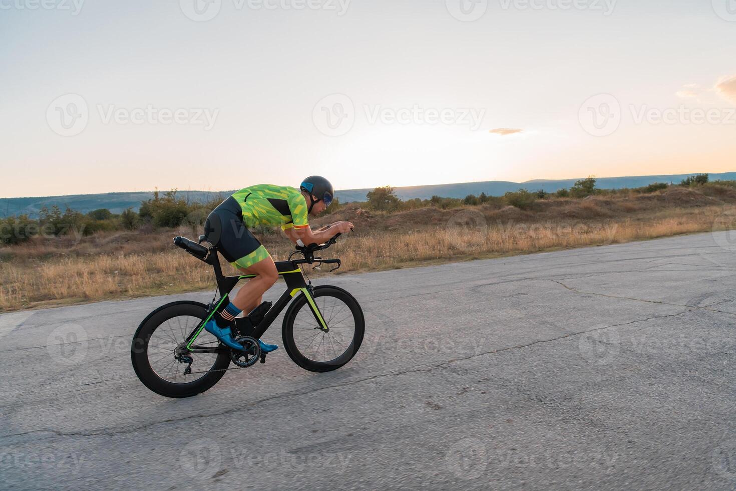 Triathlete riding his bicycle during sunset, preparing for a marathon. The warm colors of the sky provide a beautiful backdrop for his determined and focused effort. photo