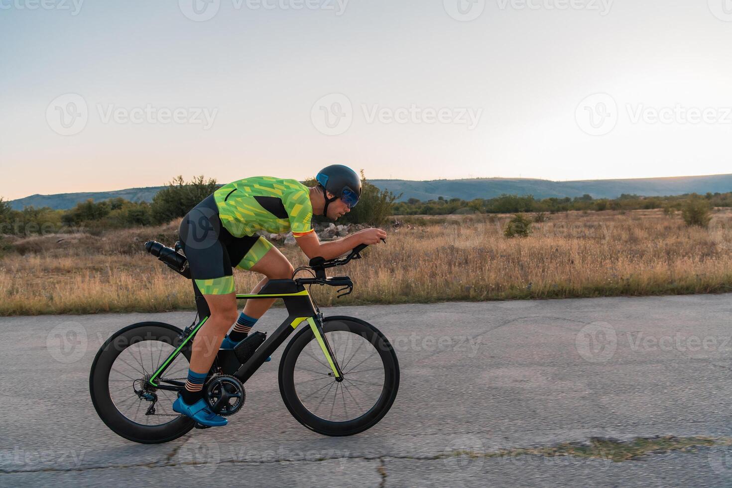 Triathlete riding his bicycle during sunset, preparing for a marathon. The warm colors of the sky provide a beautiful backdrop for his determined and focused effort. photo