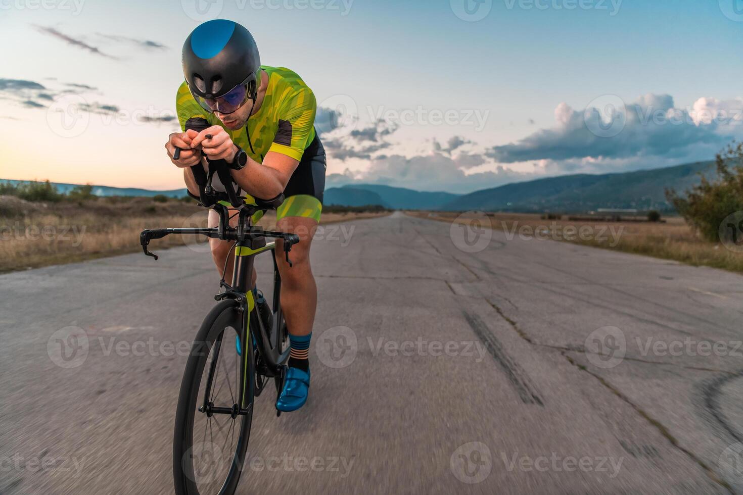 Triathlete riding his bicycle during sunset, preparing for a marathon. The warm colors of the sky provide a beautiful backdrop for his determined and focused effort. photo