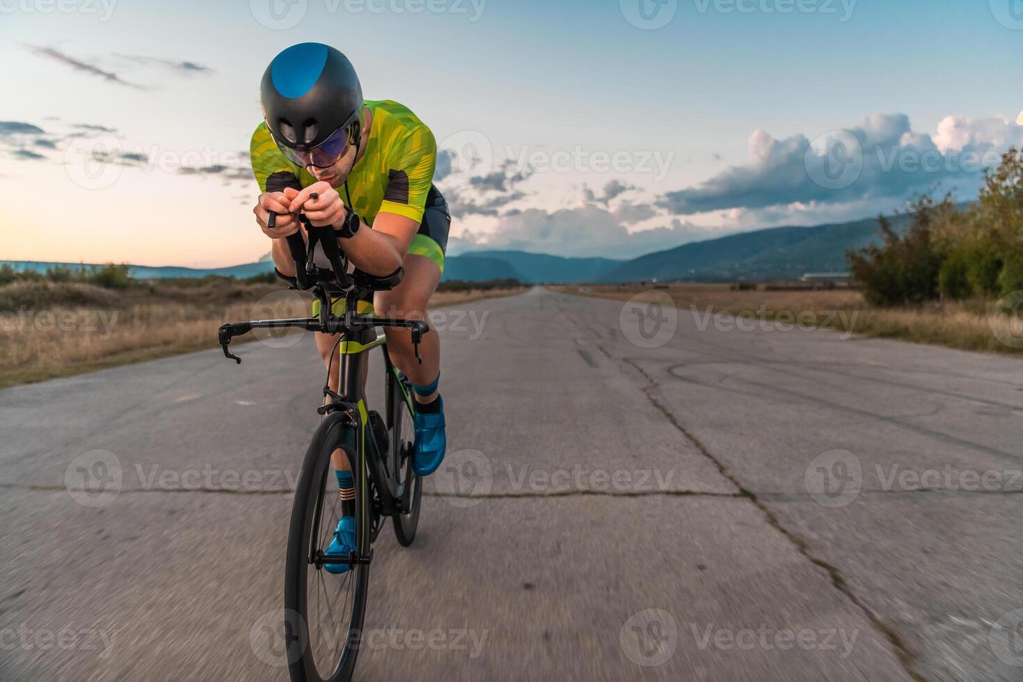 Triathlete riding his bicycle during sunset, preparing for a marathon. The warm colors of the sky provide a beautiful backdrop for his determined and focused effort. photo