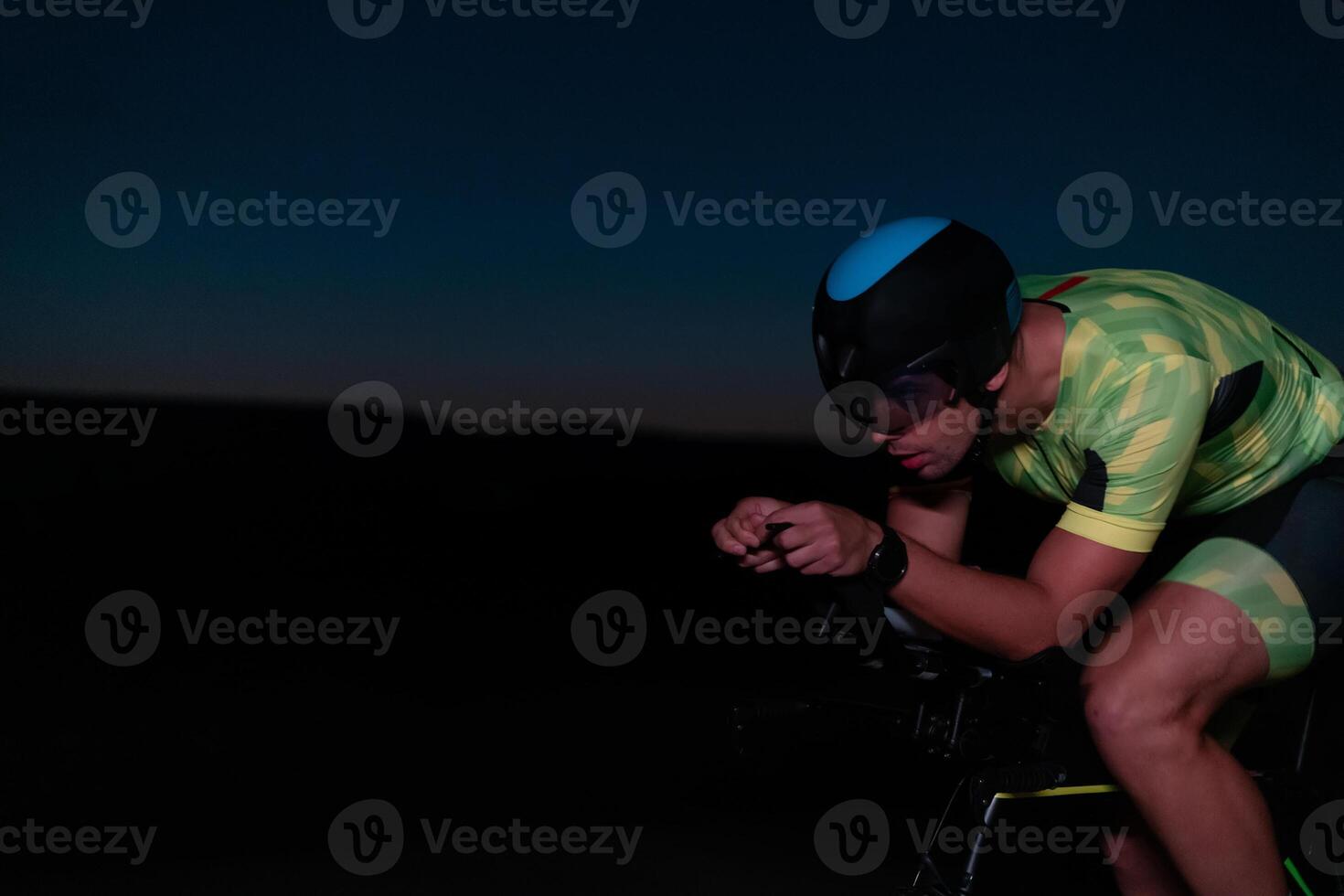 A triathlete rides his bike in the darkness of night, pushing himself to prepare for a marathon. The contrast between the darkness and the light of his bike creates a sense of drama and highlights the photo
