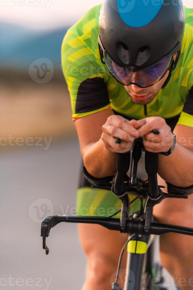 Close up photo of triathlete riding his bicycle during sunset, preparing for a marathon. The warm colors of the sky provide a beautiful backdrop for his determined and focused effort.