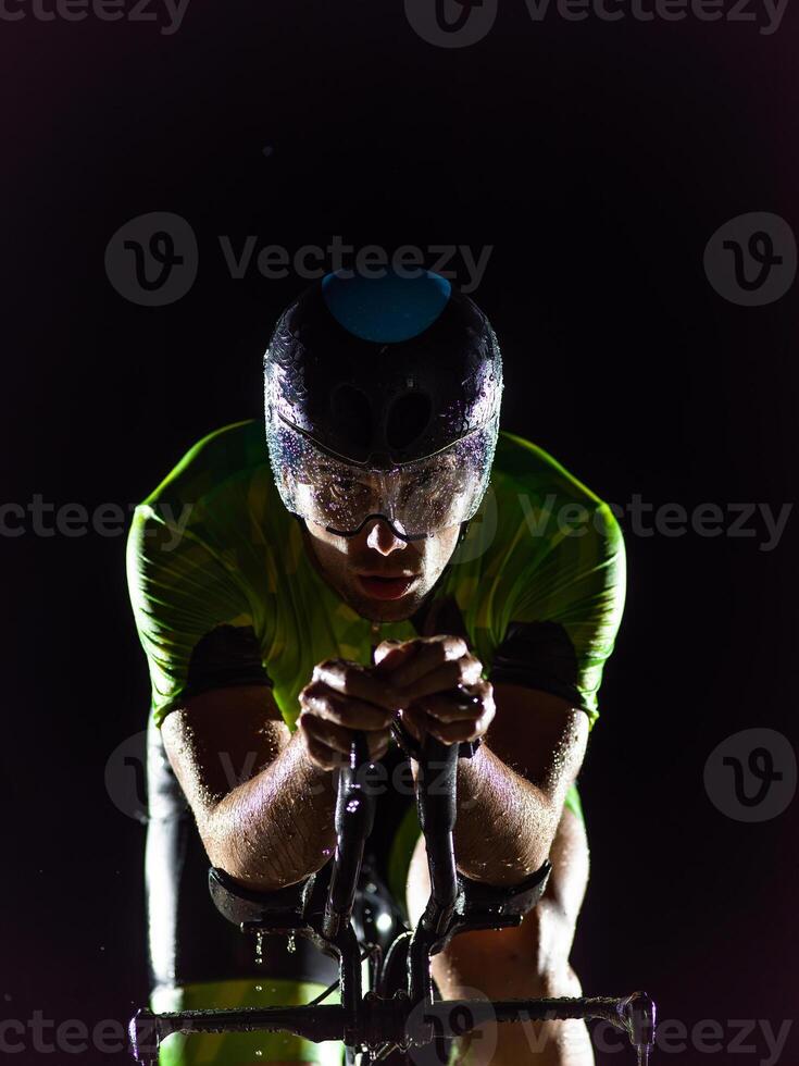 A triathlete rides his bike in the darkness of night, pushing himself to prepare for a marathon. The contrast between the darkness and the light of his bike creates a sense of drama and highlights the photo