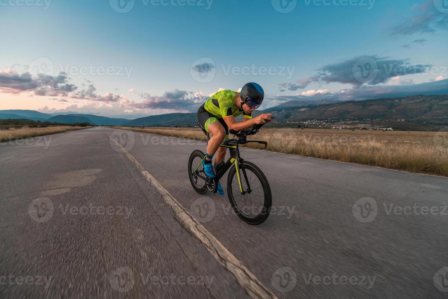 Triathlete riding his bicycle during sunset, preparing for a marathon. The warm colors of the sky provide a beautiful backdrop for his determined and focused effort. photo