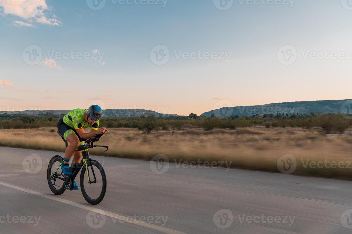 Triathlete riding his bicycle during sunset, preparing for a marathon. The warm colors of the sky provide a beautiful backdrop for his determined and focused effort. photo