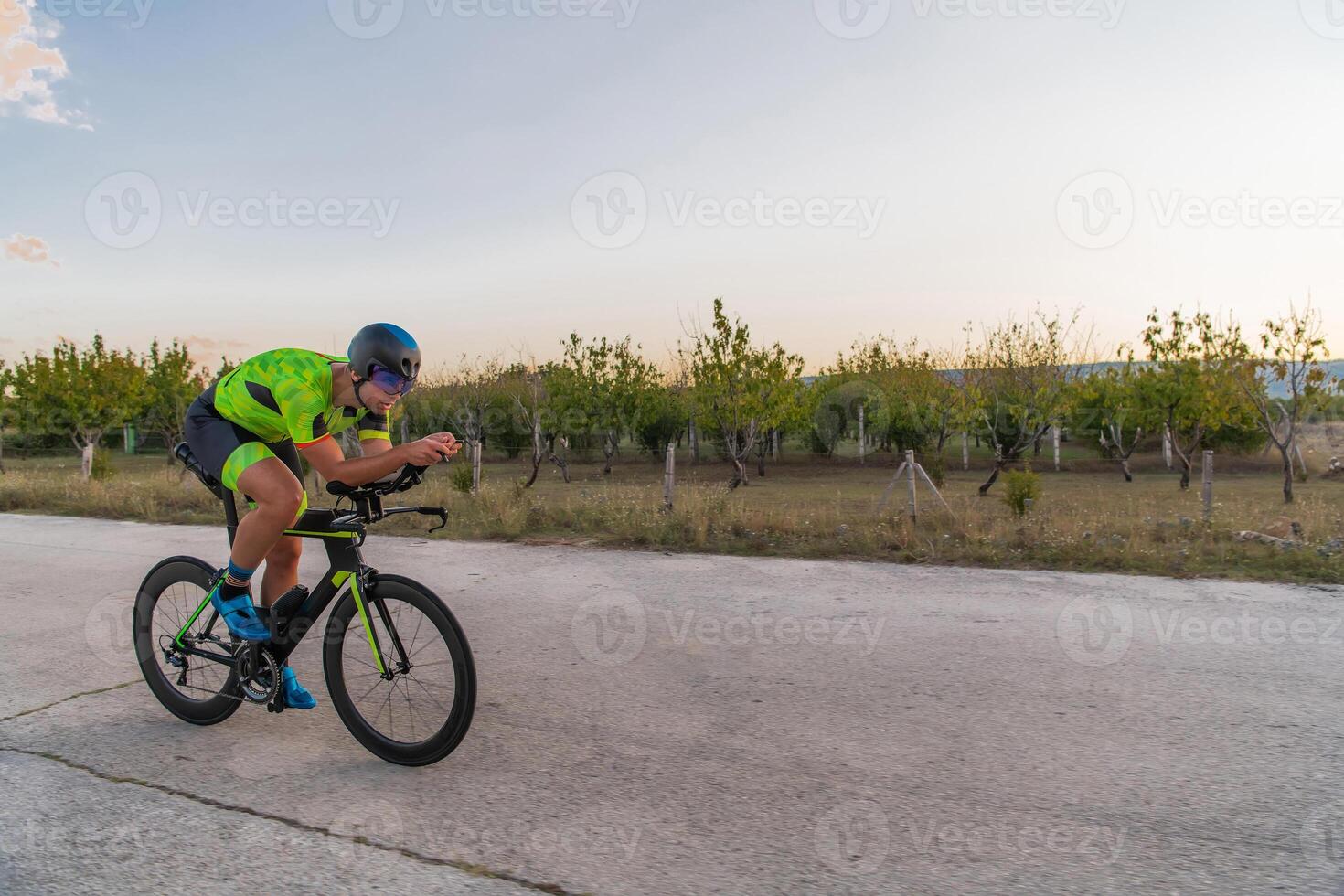 Triathlete riding his bicycle during sunset, preparing for a marathon. The warm colors of the sky provide a beautiful backdrop for his determined and focused effort. photo