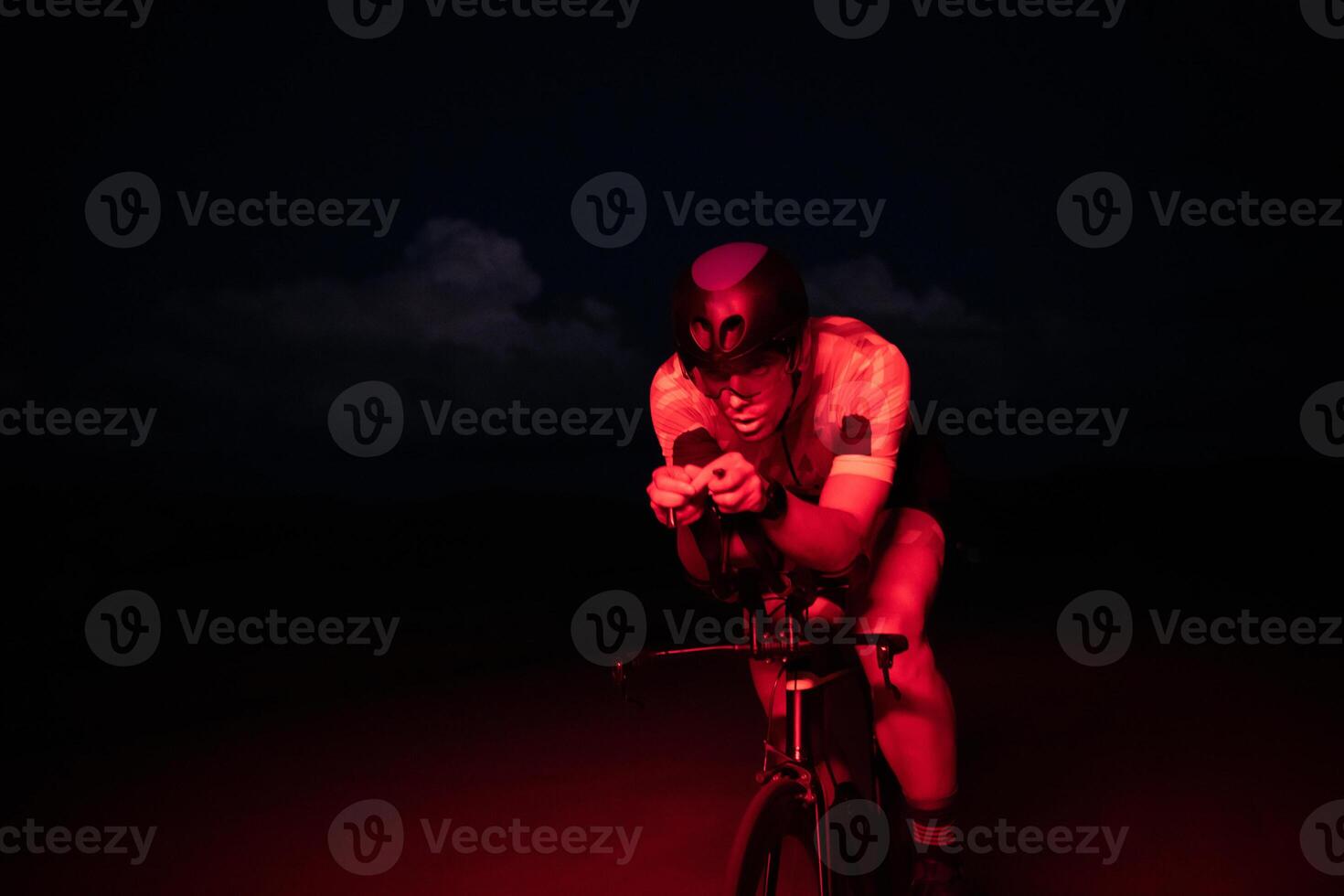 A triathlete rides his bike in the darkness of night, pushing himself to prepare for a marathon. The contrast between the darkness and the light of his bike creates a sense of drama and highlights the photo