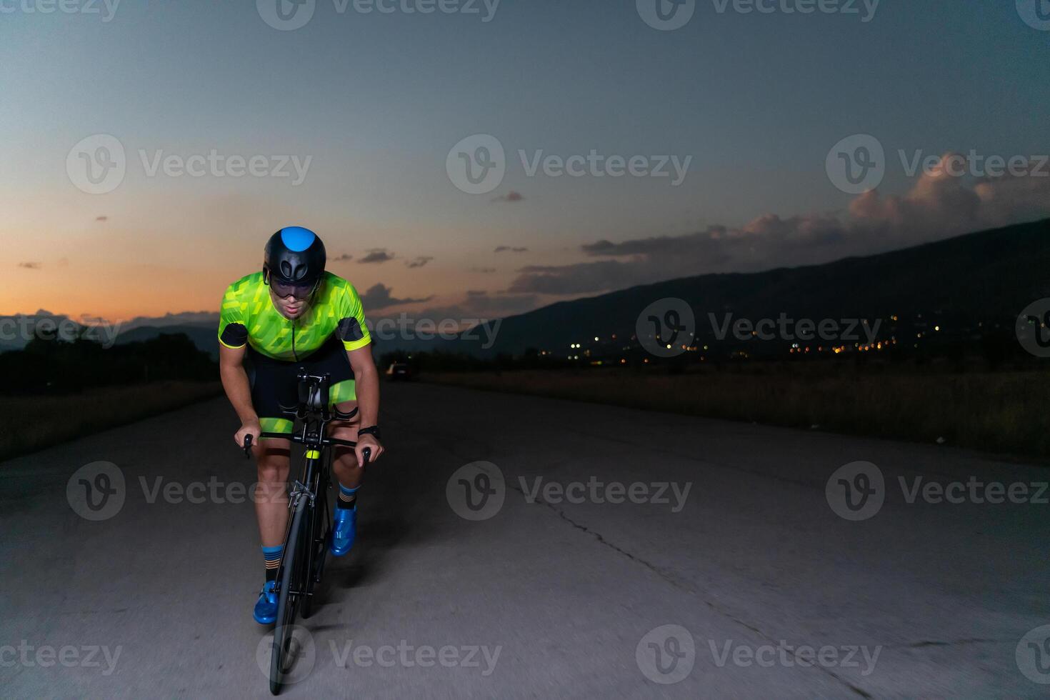 A triathlete rides his bike in the darkness of night, pushing himself to prepare for a marathon. The contrast between the darkness and the light of his bike creates a sense of drama and highlights the photo