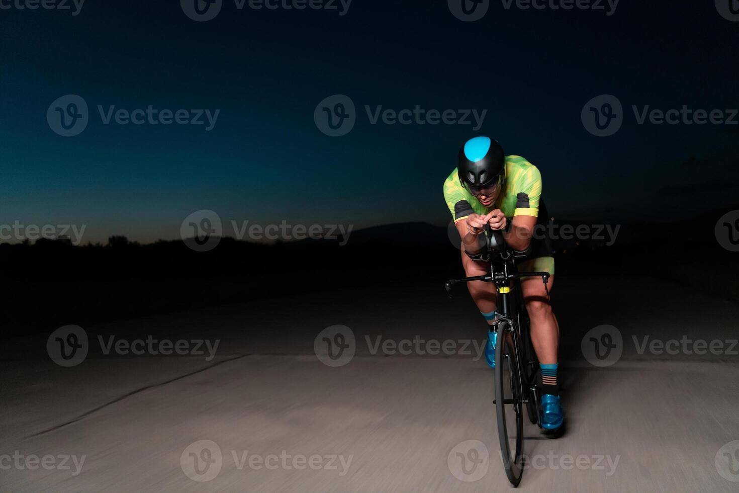 A triathlete rides his bike in the darkness of night, pushing himself to prepare for a marathon. The contrast between the darkness and the light of his bike creates a sense of drama and highlights the photo
