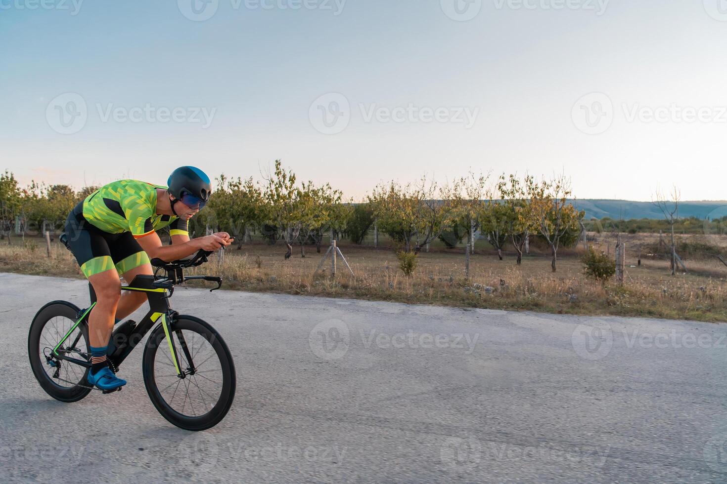 Triathlete riding his bicycle during sunset, preparing for a marathon. The warm colors of the sky provide a beautiful backdrop for his determined and focused effort. photo