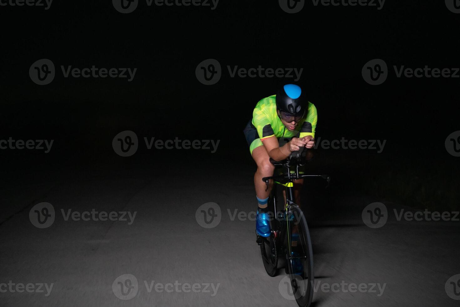 A triathlete rides his bike in the darkness of night, pushing himself to prepare for a marathon. The contrast between the darkness and the light of his bike creates a sense of drama and highlights the photo