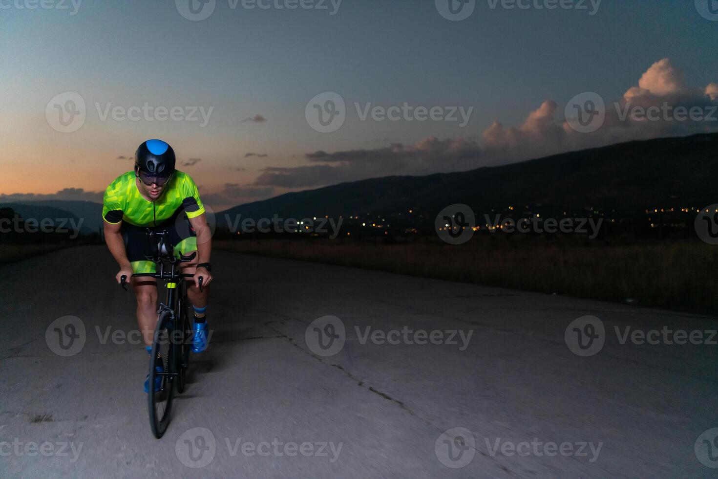 A triathlete rides his bike in the darkness of night, pushing himself to prepare for a marathon. The contrast between the darkness and the light of his bike creates a sense of drama and highlights the photo