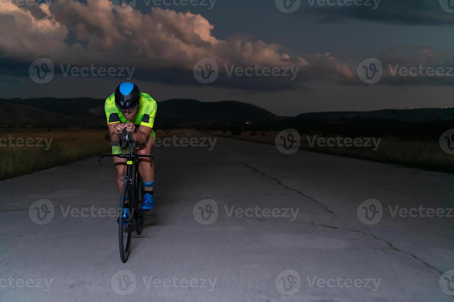 A triathlete rides his bike in the darkness of night, pushing himself to prepare for a marathon. The contrast between the darkness and the light of his bike creates a sense of drama and highlights the photo