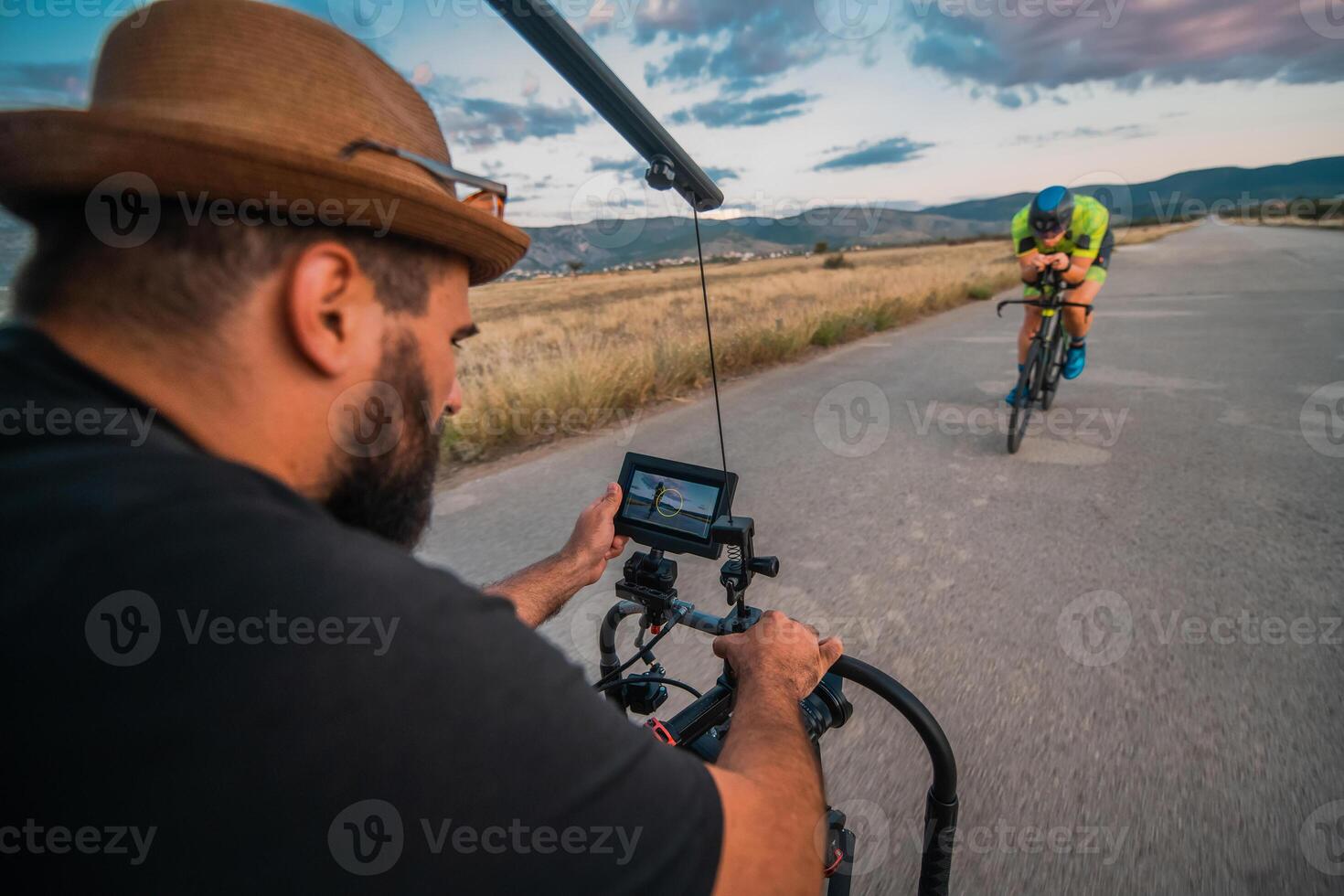 A videographer recording a triathlete riding his bike preparing for an upcoming marathon.Athlete's physical endurance and the dedication required to succeed in the sport. photo