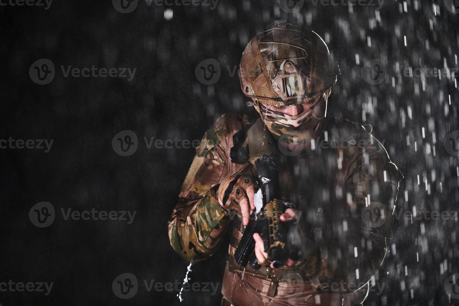 Army soldier in Combat Uniforms with an assault rifle, plate carrier and combat helmet going on a dangerous mission on a rainy night. photo