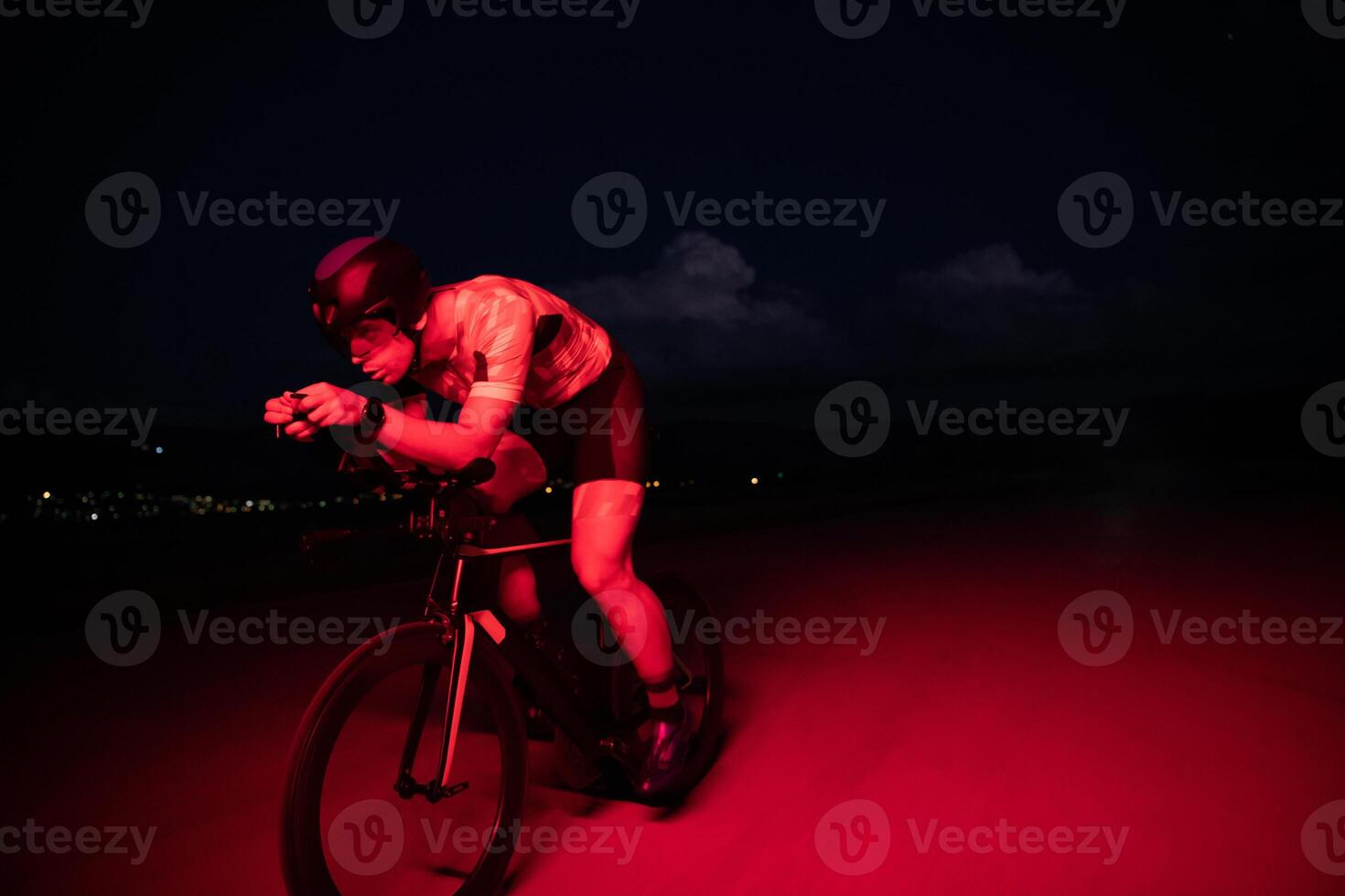 A triathlete rides his bike in the darkness of night, pushing himself to prepare for a marathon. The contrast between the darkness and the light of his bike creates a sense of drama and highlights the photo