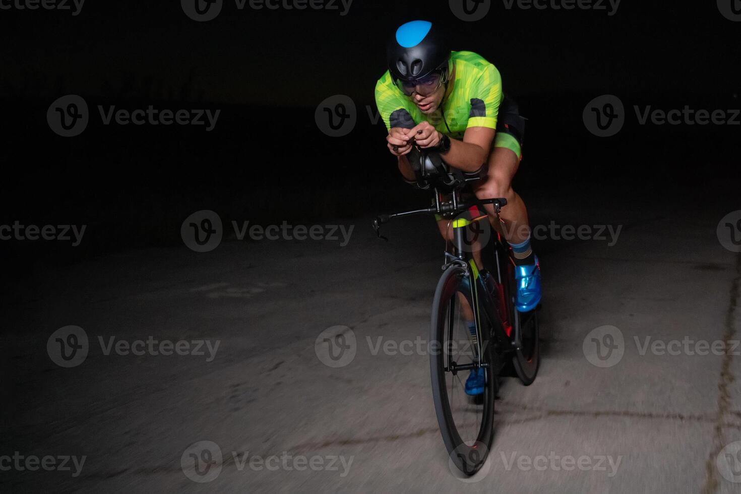 A triathlete rides his bike in the darkness of night, pushing himself to prepare for a marathon. The contrast between the darkness and the light of his bike creates a sense of drama and highlights the photo