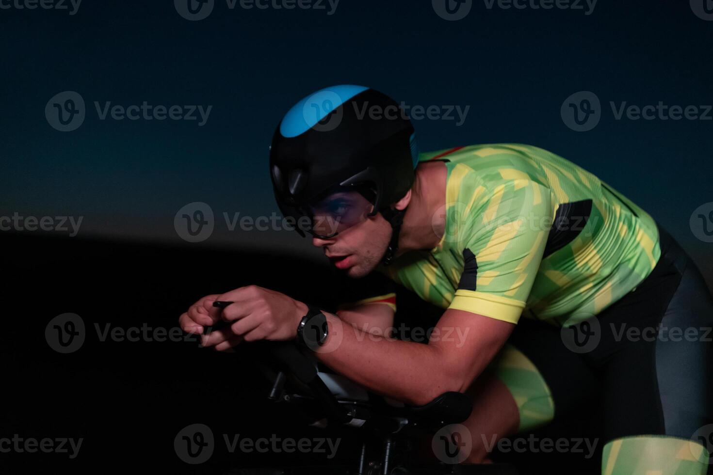 A triathlete rides his bike in the darkness of night, pushing himself to prepare for a marathon. The contrast between the darkness and the light of his bike creates a sense of drama and highlights the photo
