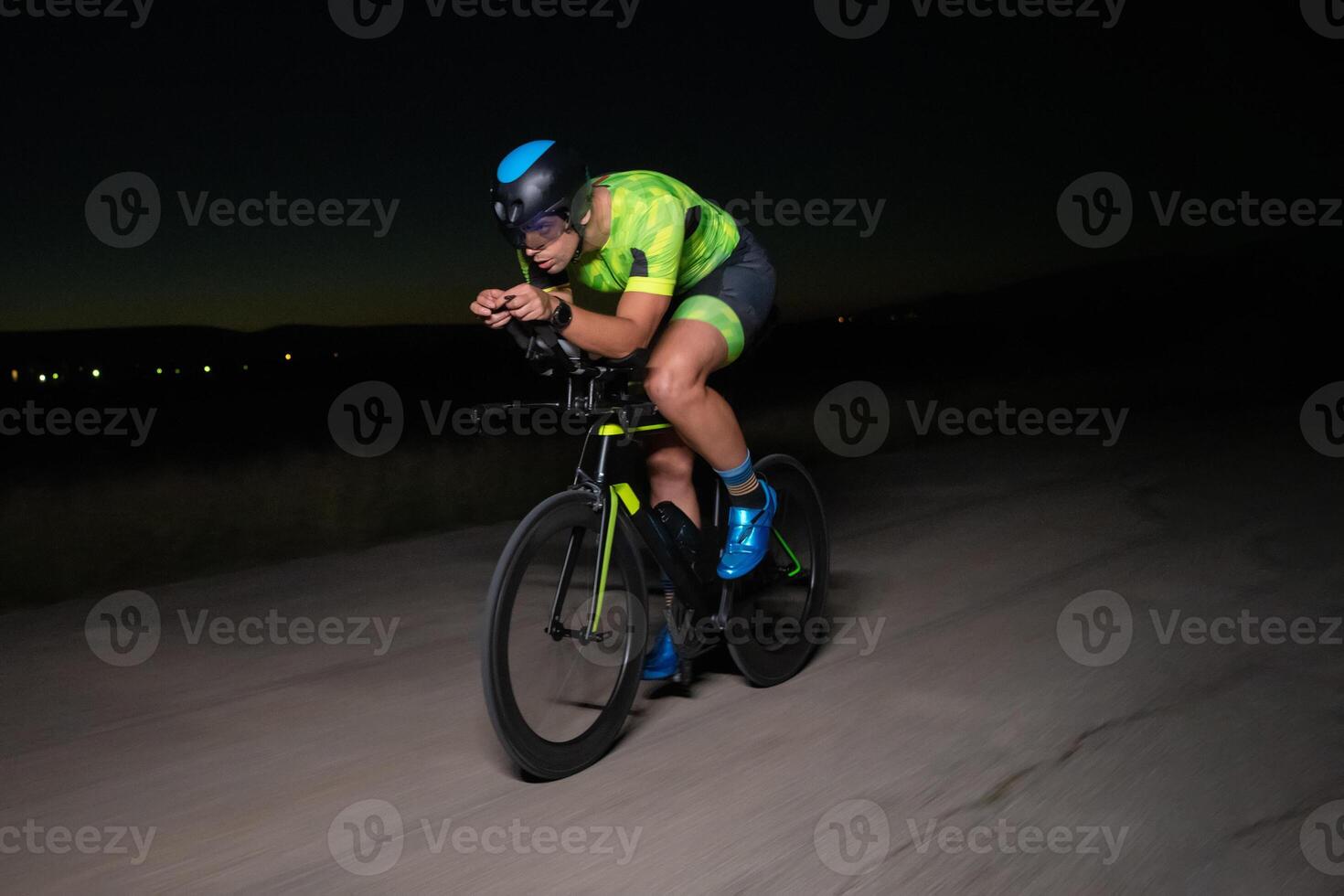 A triathlete rides his bike in the darkness of night, pushing himself to prepare for a marathon. The contrast between the darkness and the light of his bike creates a sense of drama and highlights the photo