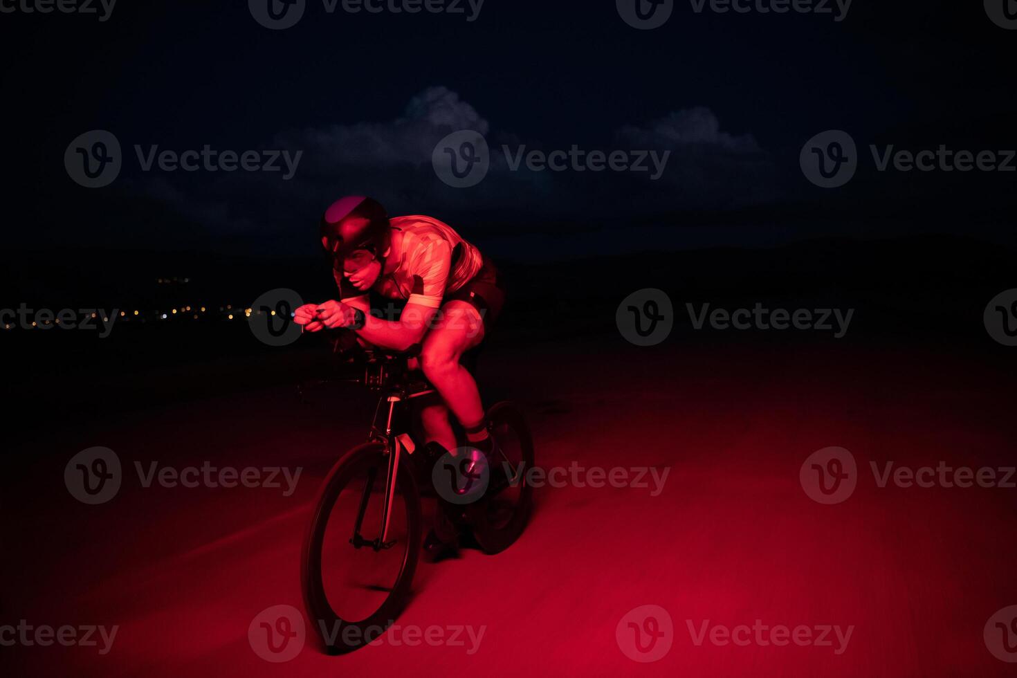 A triathlete rides his bike in the darkness of night, pushing himself to prepare for a marathon. The contrast between the darkness and the light of his bike creates a sense of drama and highlights the photo