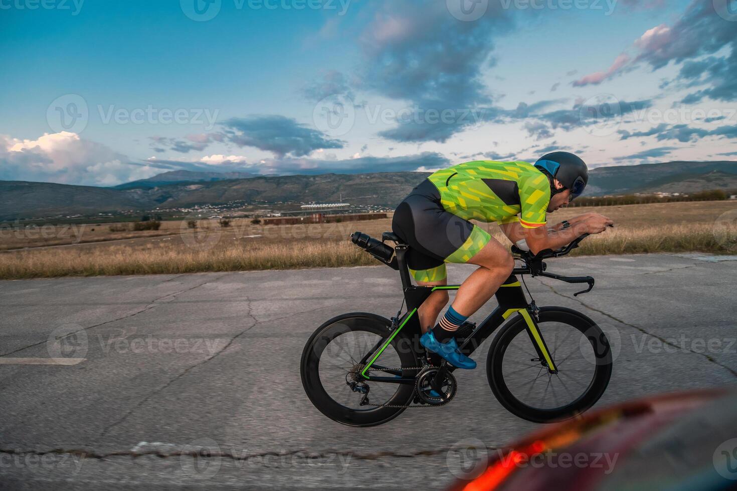 Triathlete riding his bicycle during sunset, preparing for a marathon. The warm colors of the sky provide a beautiful backdrop for his determined and focused effort. photo