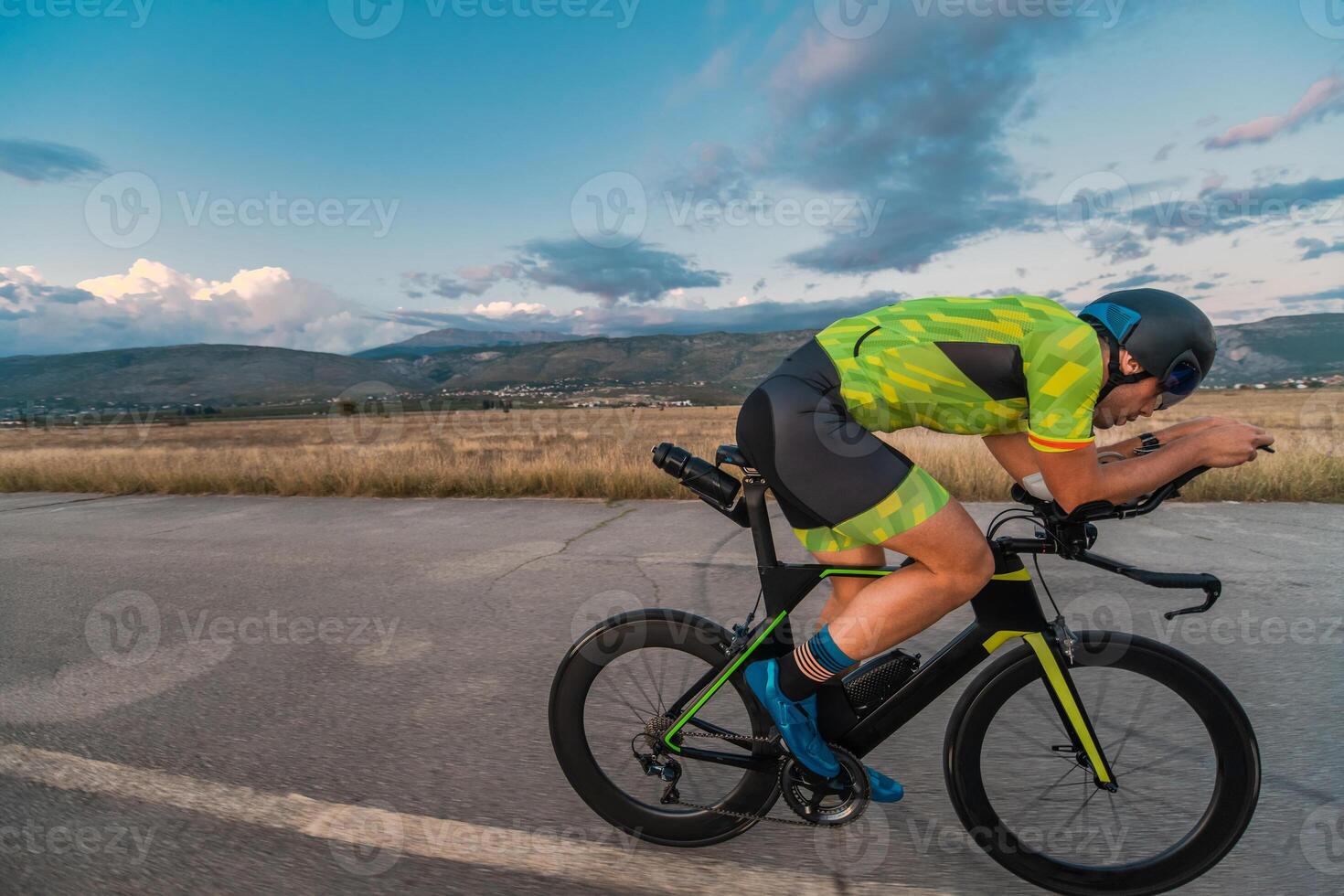 Triathlete riding his bicycle during sunset, preparing for a marathon. The warm colors of the sky provide a beautiful backdrop for his determined and focused effort. photo