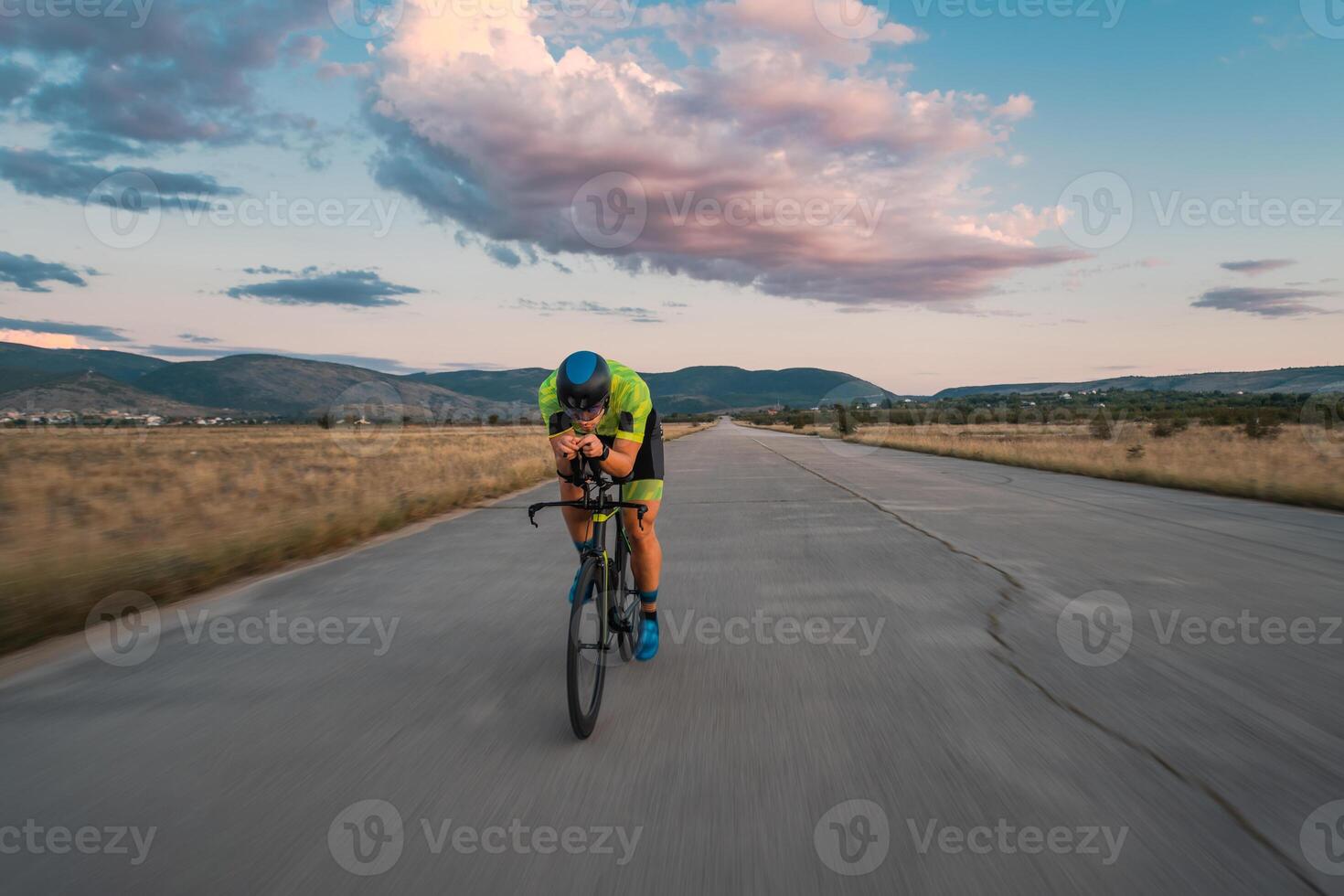 Triathlete riding his bicycle during sunset, preparing for a marathon. The warm colors of the sky provide a beautiful backdrop for his determined and focused effort. photo