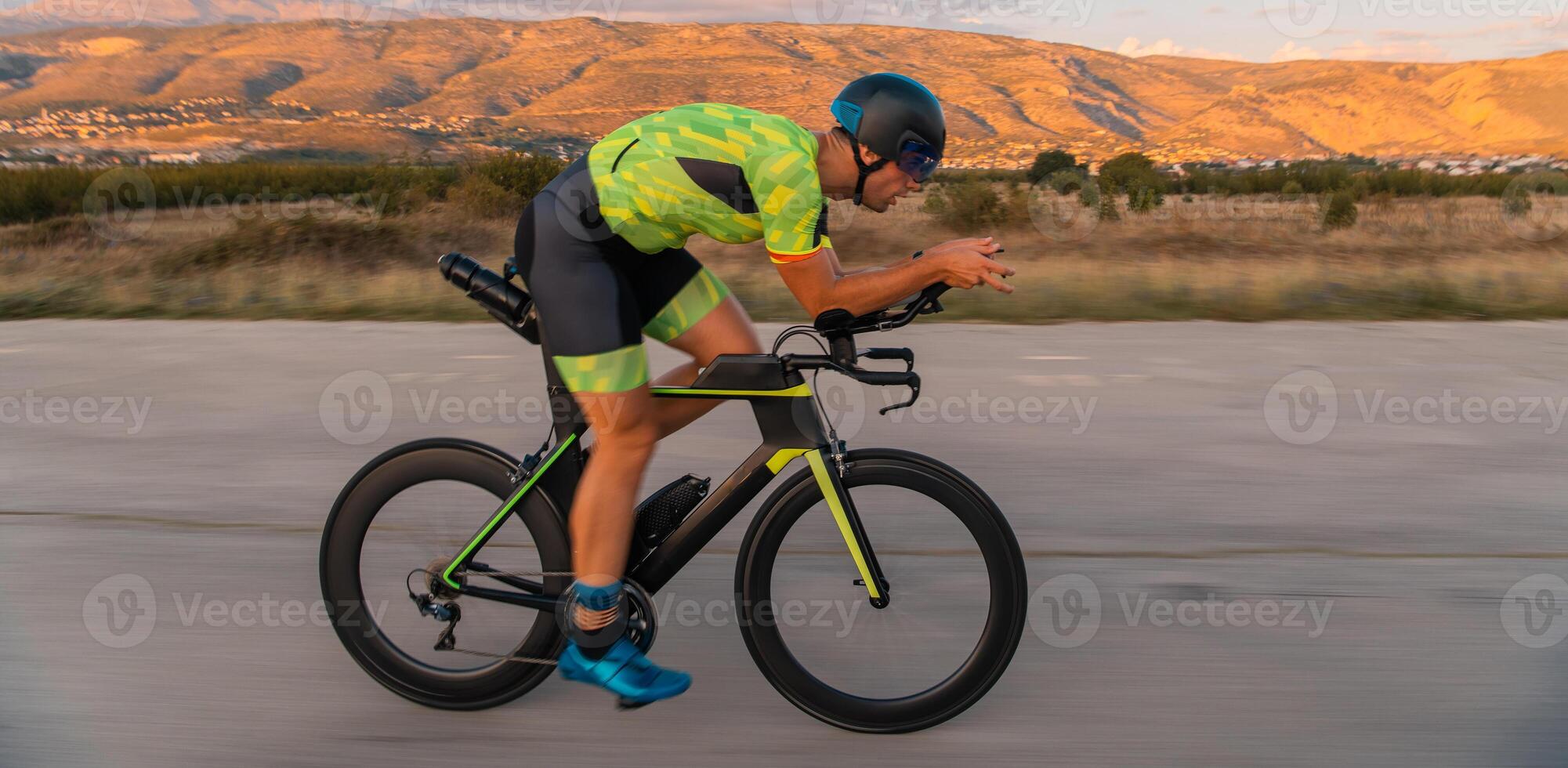 Triathlete riding his bicycle during sunset, preparing for a marathon. The warm colors of the sky provide a beautiful backdrop for his determined and focused effort. photo