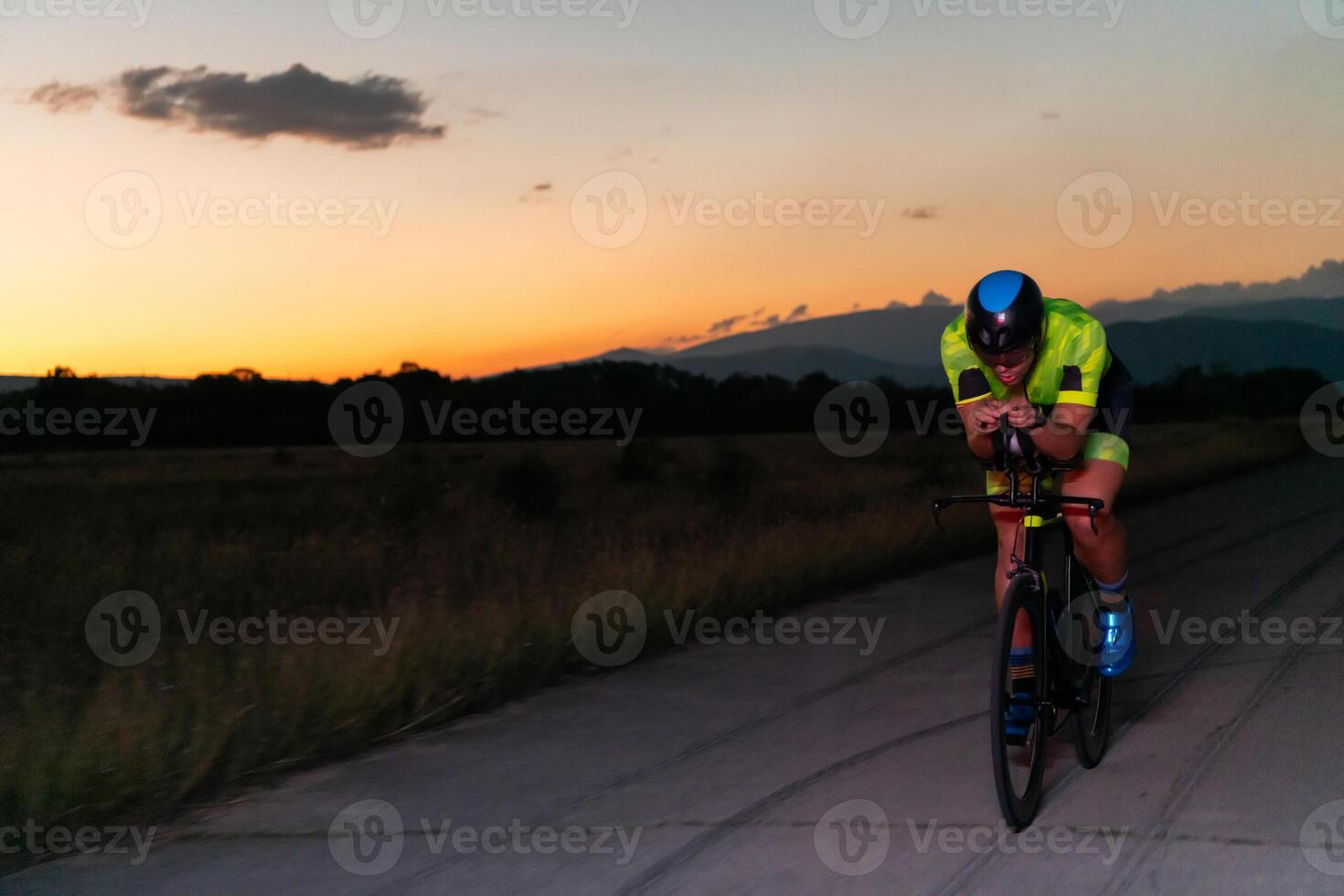 A triathlete rides his bike in the darkness of night, pushing himself to prepare for a marathon. The contrast between the darkness and the light of his bike creates a sense of drama and highlights the photo