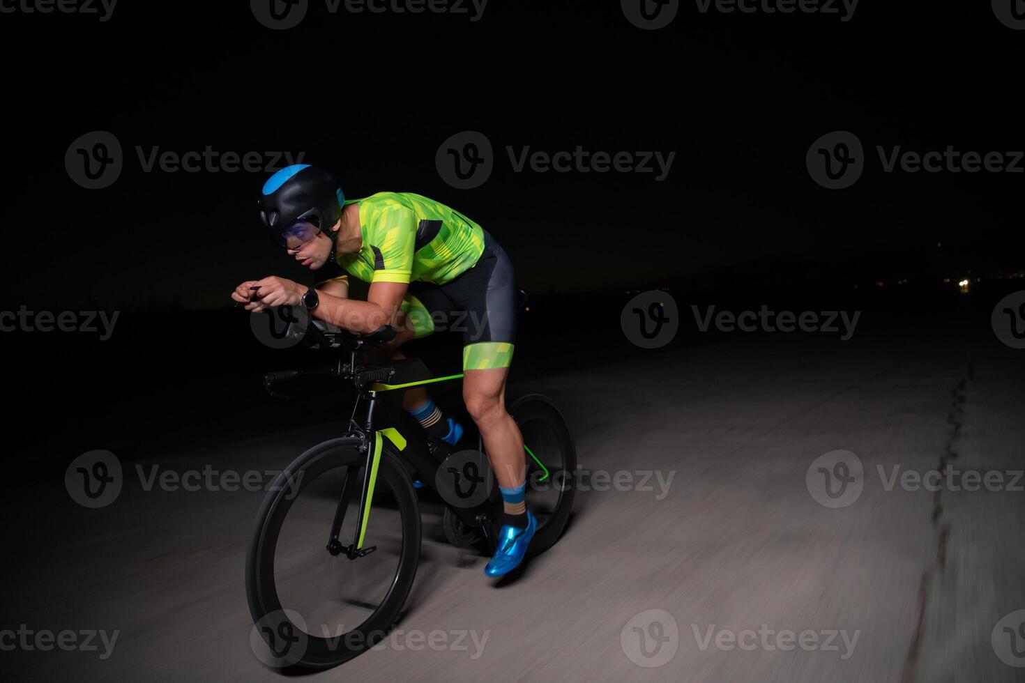A triathlete rides his bike in the darkness of night, pushing himself to prepare for a marathon. The contrast between the darkness and the light of his bike creates a sense of drama and highlights the photo