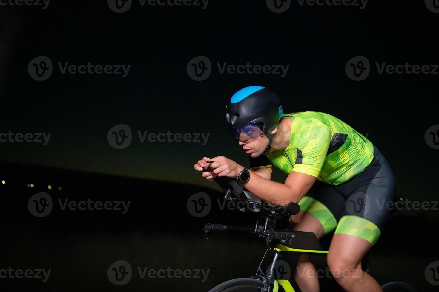 A triathlete rides his bike in the darkness of night, pushing himself to prepare for a marathon. The contrast between the darkness and the light of his bike creates a sense of drama and highlights the photo