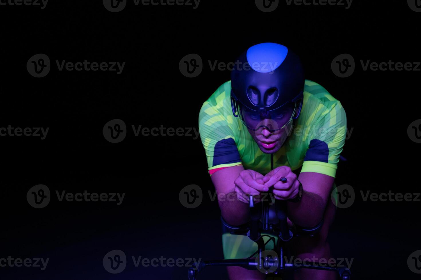 A triathlete rides his bike in the darkness of night, pushing himself to prepare for a marathon. The contrast between the darkness and the light of his bike creates a sense of drama and highlights the photo