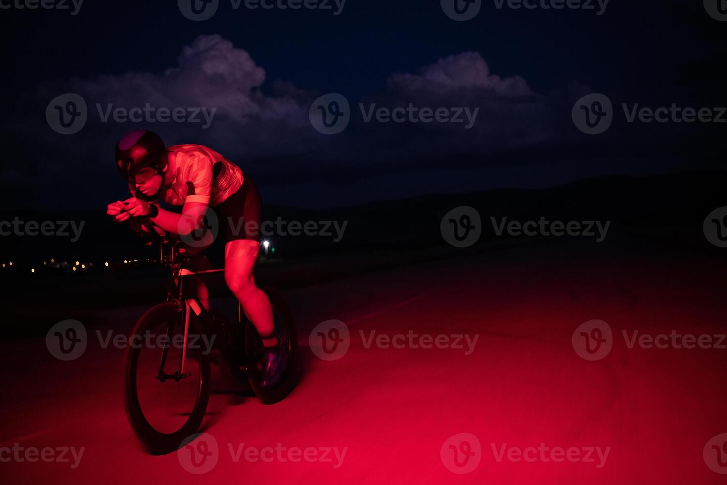 A triathlete rides his bike in the darkness of night, pushing himself to prepare for a marathon. The contrast between the darkness and the light of his bike creates a sense of drama and highlights the photo