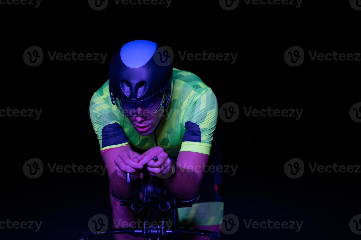 A triathlete rides his bike in the darkness of night, pushing himself to prepare for a marathon. The contrast between the darkness and the light of his bike creates a sense of drama and highlights the photo