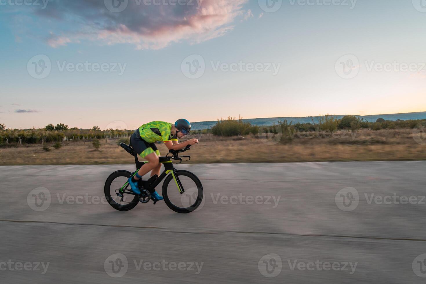 Triathlete riding his bicycle during sunset, preparing for a marathon. The warm colors of the sky provide a beautiful backdrop for his determined and focused effort. photo